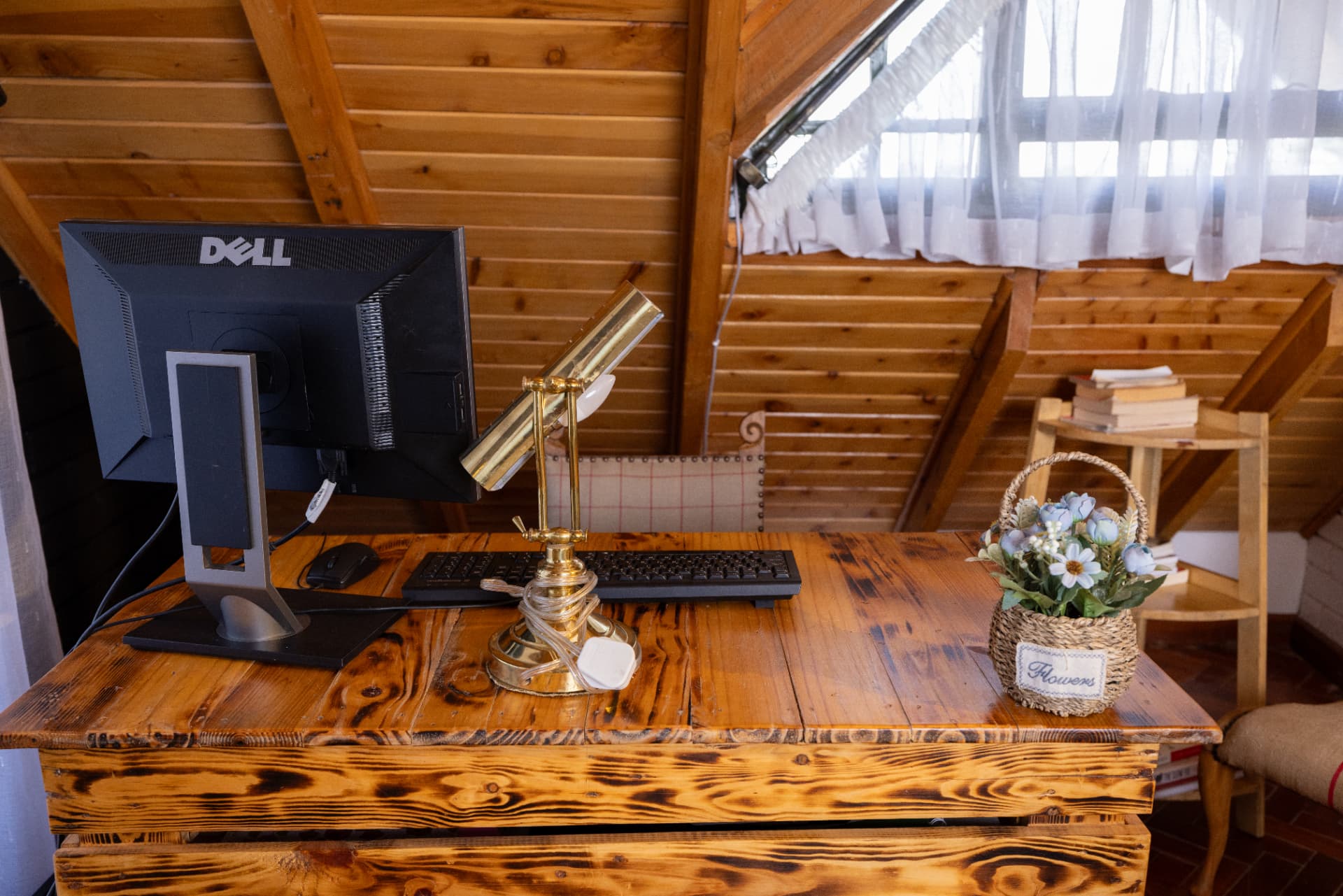 Desk corner in a timber loft with scorched reclaimed pine desk, brass banker's lamp, books and a basket of flowers